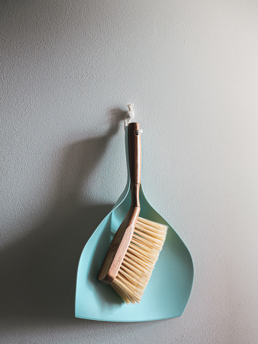 A wooden brush and aqua dustpan on a pale wall